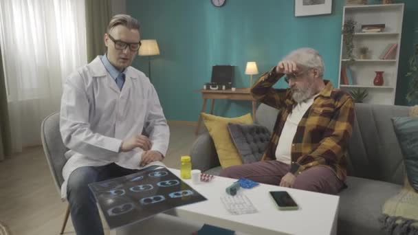 一个医生在家中检查病人病情的全片录像 他正在和一个有健康问题的老年人谈话 还在检查X光片 保健系统 医疗服务 — 图库视频影像
