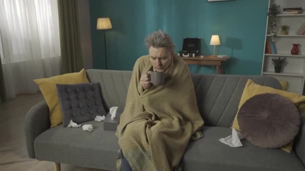 ソファーに座っている中年の男のビデオでズーム 毛布に包まれたソファー 彼はインフルエンザや風邪を持っているかのように咳 ティッシュに囲まれ お茶を飲む 病気について Hdrについて — ストック動画