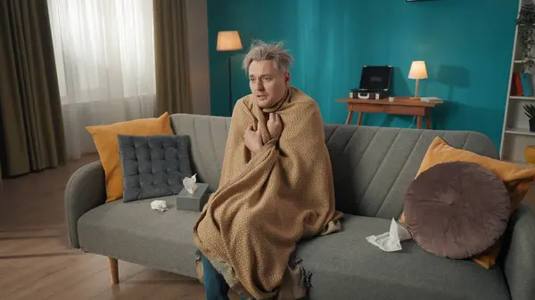 一个中年男人坐在沙发上 裹着毛毯的沙发上 周围布满了流鼻涕的纸巾 保健系统 医疗问题 — 图库照片