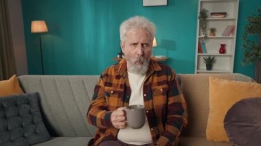 Yaşlı, emekli bir adamın, bir koltukta oturan yaşlı bir vatandaşın videosunu büyüt, kanepe, çay içerken aniden güçlü bir diş ağrısı, acı hisseder. Sağlık sistemi, sağlık hizmetleri, reklam.