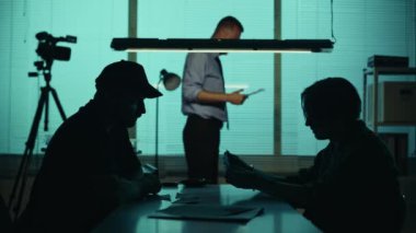 Siluet, şüpheli, fail, sorgu odasında dedektif ve polisle birlikte oturan bir mahkumun orta ölçekli videosu. İtirafı almaya çalışıyorlar. Gerçek suç, belgesel, yaratıcı içerik.