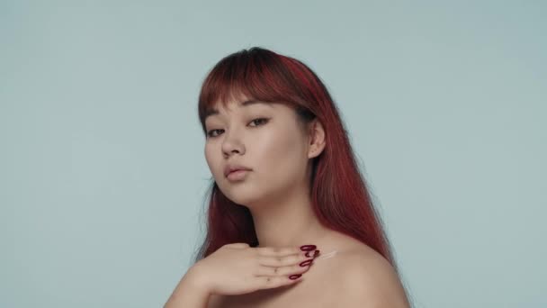 一个有着红色染发和裸体妆容的年轻的神童女子凝视着相机 用护发素在她的身体上涂奶油的特写视频 化妆品 护肤广告 — 图库视频影像