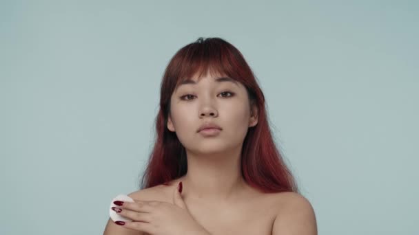 赤い染められた髪と裸の化粧をした若いセミナーの女性のクローズアップされたスローモーションビデオは 彼女の襟の向こうに綿のパッドを移動します ビューティー スキンケア広告 — ストック動画