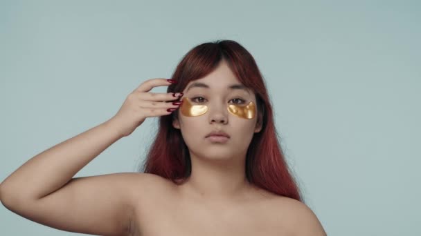 一个有着红色染发和裸体妆容的年轻的神童女人在她的眼睛下面修整和拍拍眼部的镜头 黑眼圈美容 化妆品 护肤广告 — 图库视频影像