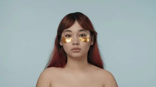 一个有着红色染发和裸体妆容的年轻女性的近照 她的眼睛下面有两个金黄色的眼罩 黑眼圈美容 化妆品 护肤广告 — 图库照片