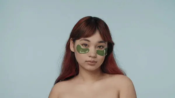 一个有着红色染发和裸体妆容的年轻女性的近照 她的眼睛下面有两个绿色的眼罩 黑眼圈美容 化妆品 护肤广告 — 图库照片
