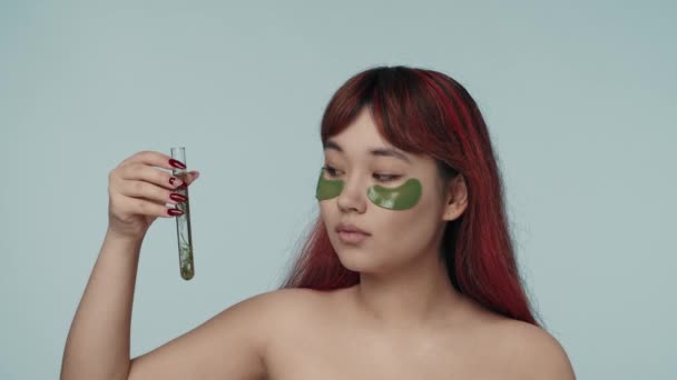 赤い染められた髪とヌードのメイクを施した若いセミナーの女性のクローズアップされたスローモーションビデオは その中に海藻を塗ったラボフラスコを示しています 美しさ 化粧品 スキンケア広告 — ストック動画