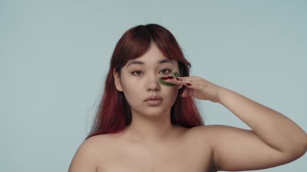 赤い染められた髪とヌードのメイクを施した若いセミナーの女性の閉じた隔離されたスローモーションビデオは 彼女の目の下にアイパッチを固定し おしゃべりします ダークサークル 美しさ 化粧品 スキンケア広告 — ストック動画