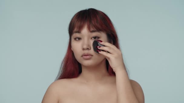 赤い染められた髪とヌードのメイクでカメラを見ている若いセミナーの女性のクローズアップされた隔離されたスローモーションビデオ ブラシで粉末化メイクを適用します 美しさ 化粧品 スキンケア広告 — ストック動画