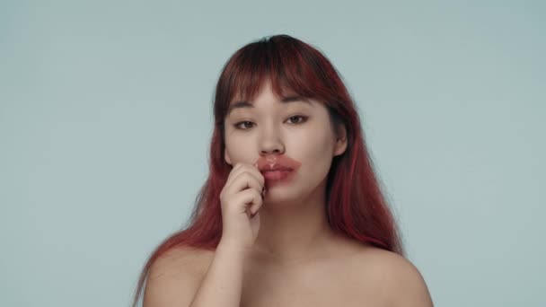 赤い染められた髪の若いセミナーの女性とヌードのメイクが唇のパッチを脱ぎ 唇をパットにしたクローズアップされたスローモーションビデオ チャッピング 乾いた唇 美しさ 化粧品 スキンケア広告 — ストック動画