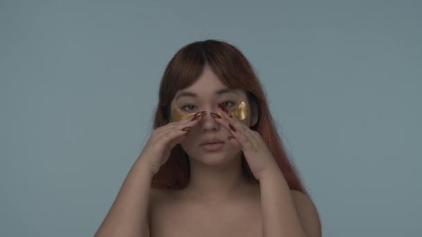 赤い染められた髪とヌードのメイクの修理と彼女の目の下に適用された眉毛を打つ若いセミナーの女性の閉じた隔離されたビデオ ダークサークル 美しさ 化粧品 スキンケア広告 — ストック動画
