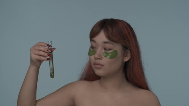 赤い染められた髪とヌードのメイクを施した若いセミナーの女性のクローズアップされたスローモーションビデオは その中に海藻を塗ったラボフラスコを示しています 美しさ 化粧品 スキンケア広告 — ストック動画