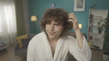 Kameraya yakın çekim yapan genç bir adam var. Sanki aynada saç kurutma makinesini tutar gibi, inceler ve kıvırcık saçlarını düzeltir. Şüpheyi, öfkeyi, huzursuzluğu gösterir. Ağır çekim. HDR BT2020 HLG Malzemesi.