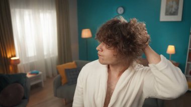 Cüppeli genç bir adamın yakın planda bir odada dikilip aynaya bakar gibi yana baktığı bir fotoğrafta. Kalın, kıvırcık saçlarını düzeltir ve düzenler. Tatminsizliği, huzursuzluğu gösterir. Saç bakımı.