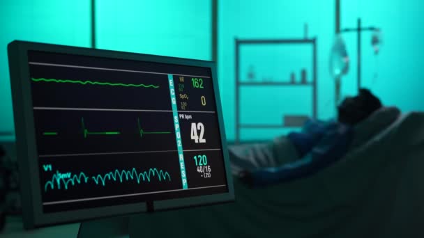 心臓と圧力率を示す意図的なケアユニットをキャプチャするクローズアップビデオ バックグラウンドで死んでいる患者の輝かしいシルエット ラインはモニターでまっすぐ行きます — ストック動画