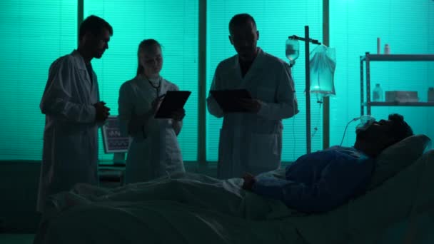3名医生站在病人身边 靠呼吸支持 昏迷中 躺在他们前面的病床上的全长轮廓录像 急性病治疗 医疗护理 — 图库视频影像