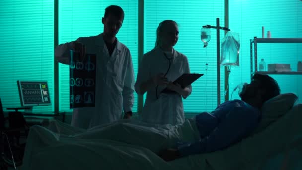 两个医生站在病人旁边躺在病床上的呼吸支撑物上的全长轮廓录像 医生们和他讨论了治疗方法 — 图库视频影像