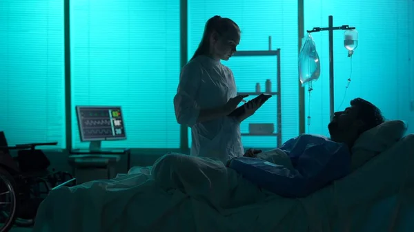Full-sized silhouette shot of a double amputee patient laying in a hospital bed. A female doctor, nurse comes in for a check-up. She talks to a patient. Hostital, surgical treatment, disability.
