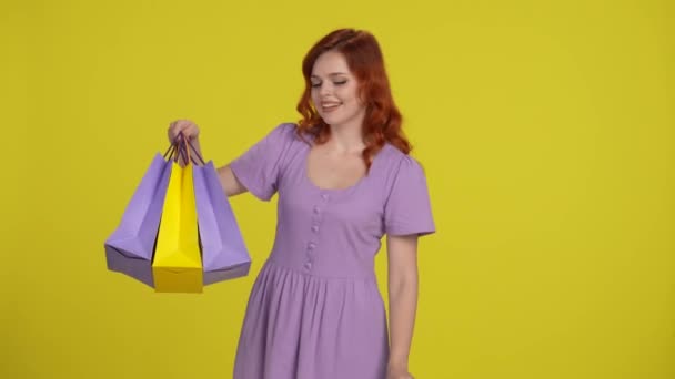 赤毛の若い女性はショッピングバッグに満足して見て ギフト券 クーポン バウチャーを示しています 黄色で孤立した若い女性 ショッピングコンセプト — ストック動画