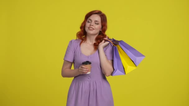 빨간머리 여자는 쇼핑백을 커피를 마시고 종이컵에서 마시고 바라보고 있습니다 노란색 — 비디오