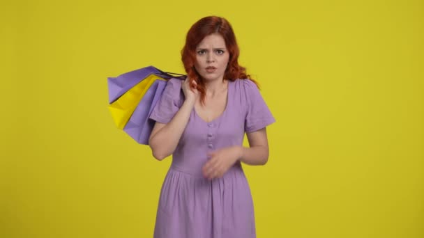 쇼핑백을 실망스러운 빨간머리 여자는 어리둥절함과 으스러기에 던집니다 노란색 배경에 스튜디오에서 — 비디오