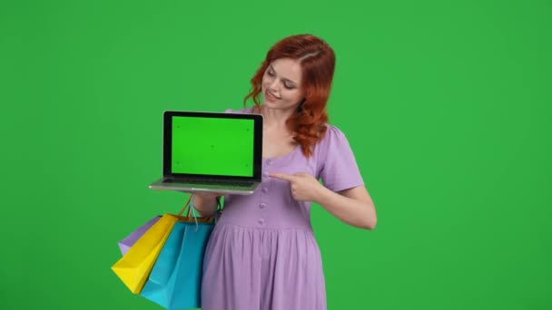 Młoda Kobieta Torbami Zakupy Wskazuje Palcem Wskazującym Zielony Ekran Laptopa — Wideo stockowe