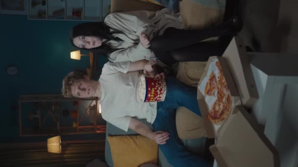 最初の愛と関係創造的なコンセプト ソファーに座ってポップコーンを食べ 映画を見ている少年と少女 少年は少女を抱きしめようとするが 彼女は断る バーティカルビデオ — ストック動画