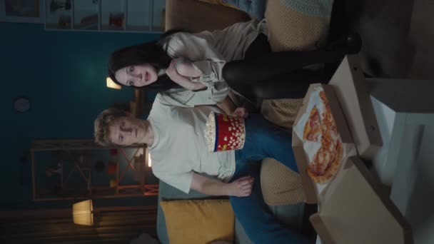 最初の愛と関係創造的なコンセプト ソファーに座ってポップコーンを食べ 映画を見ている少年と少女 少年は恥ずかしげに女の子の肩に手を置き 少女はハグを受け入れる バーティカルビデオ — ストック動画