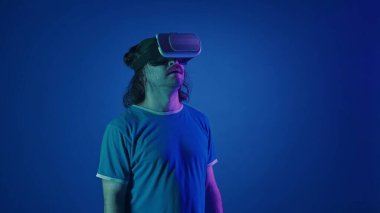 Stüdyoda pembe ve yeşil ışıklı mavi arka planda sanal gerçeklik gözlüğü takan bir adam.