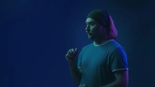 目に見えないスクリーンで働く集中した男 ピンクとグリーンネオンライトの青い背景にあるスタジオでヘッドバンドのマッサージされた男の肖像画 — ストック写真