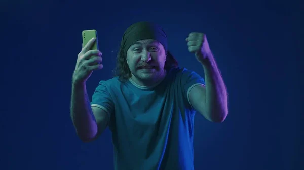 Joyful Man Makes Victory Gesture Man Smartphone His Hands Studio — Stock Photo, Image