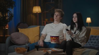 İlk ilişkiler yaratıcı konsept. Boş zamanlarını geçiren genç bir çiftin portresi. Oğlan ve kız kanepede oturup patlamış mısır yiyor ve televizyonda bir şeyler izliyorlar..