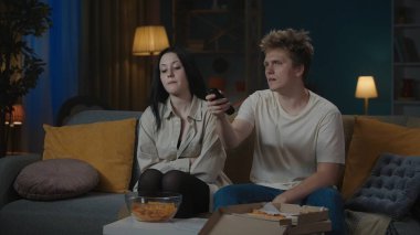 İlk ilişkiler yaratıcı konsept. Boş zamanlarını geçiren genç bir çiftin portresi. Oğlan ve kız kanepede oturur televizyon izler, pizza yer, mutsuz yüz ifadeleri takınırlar..