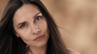 Orta yaşlı, çekici, siyah düz saçlı bir kadının yakın çekimi. Başını hafifçe eğiyor ve dikkatle kameraya bakıyor. Rüzgar onun üzerine esiyor, saçlarını geliştiriyor..