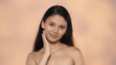 Güzellik ve cilt bakımı yaratıcı bir kavram. Çekici genç modelin yakın çekim stüdyo çekimi. Güzel Asyalı kız doğal makyajlı ve uzun saçlı yüzüne dokunan yumuşak tenli ve gülümseyen..