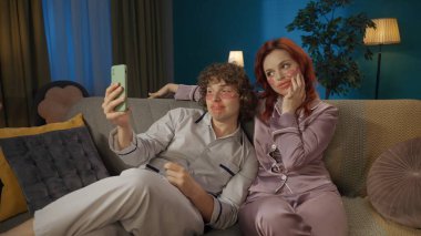 Güzellik ve sağlıklı ilişkiler reklam konsepti. Birlikte zaman geçiren genç bir çiftin portresi. Kadın ve erkek kanepede oturuyor, göz bantları takıyor, selfie çekiyorlar..