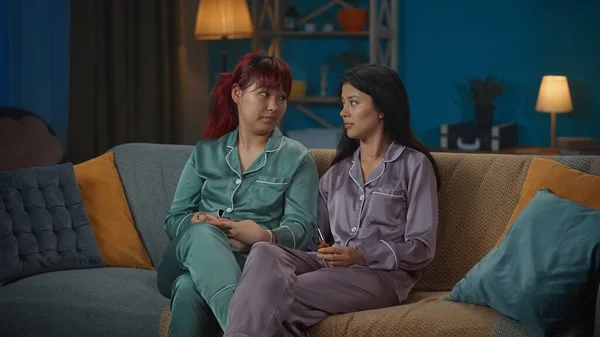 在一张中等全景的照片中 两个穿着睡衣的年轻女子坐在房间的沙发上 一边画指甲 一边谈论着一些事情 女孩之夜 过夜者 兄弟姐妹 — 图库照片