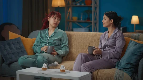 照片中 两个身穿睡衣的年轻女子坐在沙发上 聊着什么 喝着咖啡 吃着纸杯蛋糕 女孩之夜 过夜者 兄弟姐妹 — 图库照片