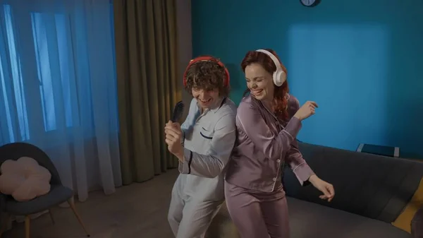 Beauty and healthy relationships advertisement concept. Portrait of young couple spending time together. Young man and woman in pajamas and headphones dancing in the living room.
