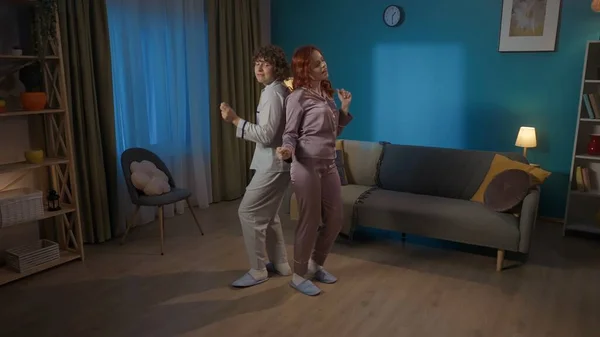 Beauty and healthy relationships advertisement concept. Portrait of young couple spending time together. Young man and woman in pajamas dancing in the living room standing back to back.