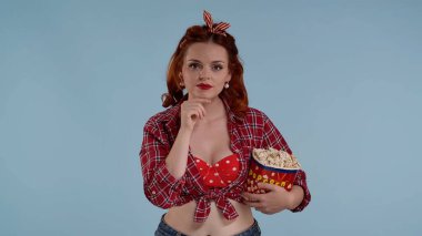 Mavi arkaplanda parlak makyajlı kızıl saçlı genç bir kadın var. Kameraya bakıyor ve elinde patlamış mısır tutuyor. Tiyatroda film izlediğini gösteriyor, dikkatli bakıyor.