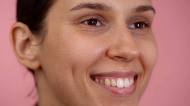 Deri dokusu ve güzellik konsepti. Çekici esmer kadın portresi. Açık gözlü, doğal ciltli, makyajsız, gülümseyen genç, beyaz bir modelin yakın çekimi..