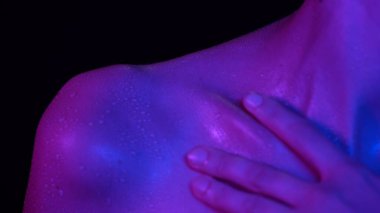 Deri dokusu ve vücut bakımı yaratıcı konsepti. Güzel bir kadın model portresi. Kafkas kadın modelin neon ışıkta vücudunun bir parçası, duştan sonra tenine su damlacıklarıyla dokunuyor..