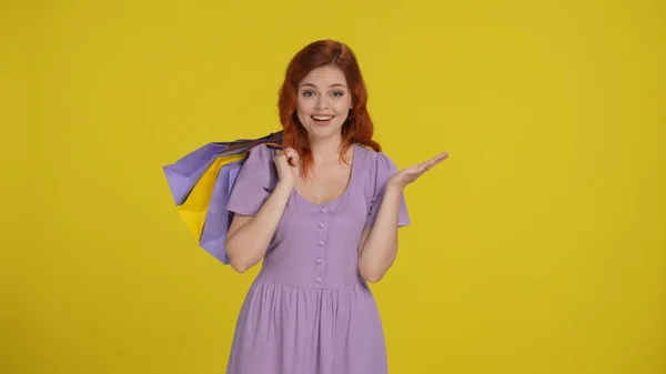 Portrait of a woman with shopping bags slung over her shoulder. Redhaired woman in the studio on a yellow background