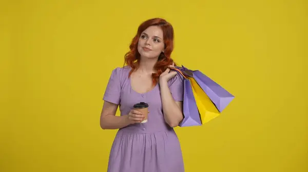 赤毛の女性はショッピングバッグと紅茶やコーヒーの紙コップを持っています 黄色の背景に隔離された夏の服の若い女性 購入の割引を販売する概念 スペースモックアップをコピー — ストック写真