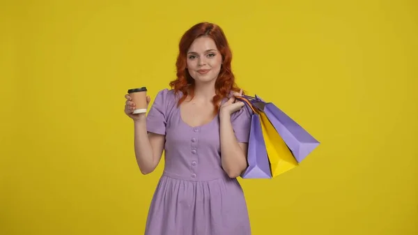 赤毛の女性はショッピングバッグと紅茶やコーヒーの紙コップを持っています 黄色の背景に隔離された夏の服の若い女性 購入の割引を販売する概念 スペースモックアップをコピー — ストック写真