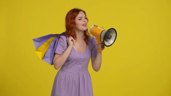 Szczęśliwa Rudowłosa Kobieta Torbami Zakupy Mówiąca Megafonu Odizolowanym Żółtym Tle — Zdjęcie stockowe