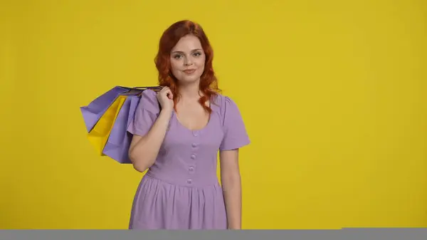 Portrait of a woman with shopping bags slung over her shoulder. Redhaired woman in the studio on a yellow background