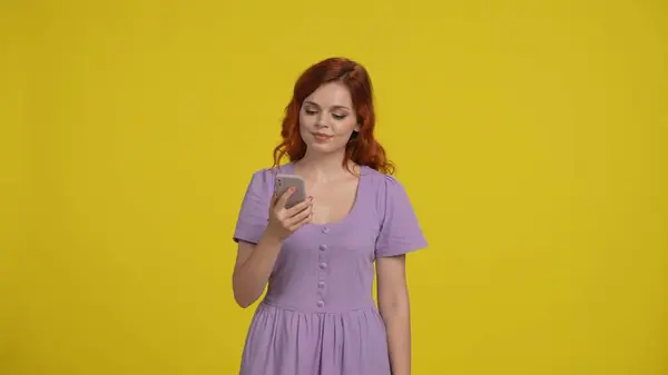 若い赤毛の女性は 黄色の背景にあるスタジオでスマートフォンを使用します — ストック写真