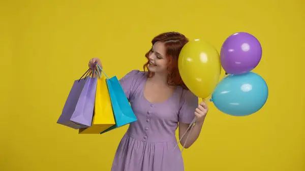 ショッピングバッグとカラフルな風船を持つ陽気で幸せな赤毛の女性 黄色の背景にあるスタジオの女性 セール ブラックフライデー — ストック写真